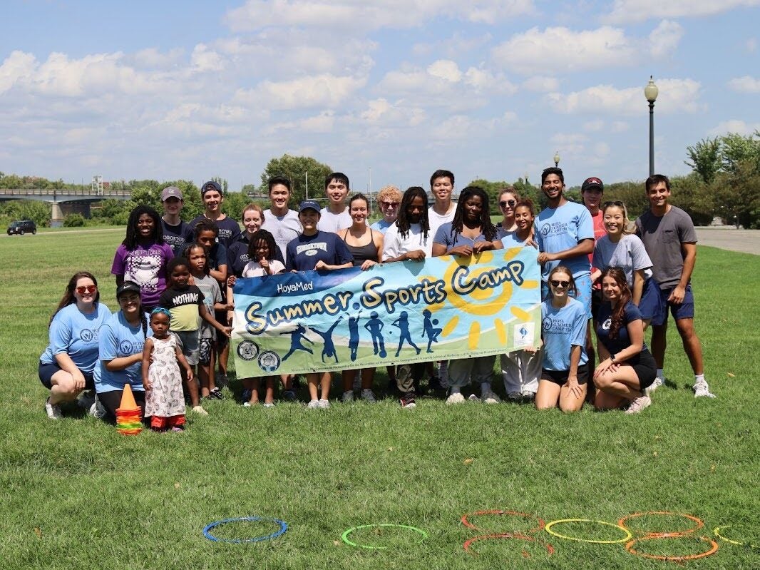 Photo of volunteers and camp attendees holding up a banner that says Summer Sports Camp.